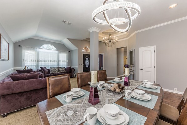 A dining area with a table set for four, surrounded by brown leather chairs, and a chandelier above.