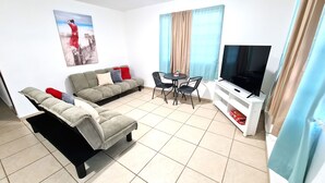 Un soggiorno con un divano, due poltrone, un tavolino, una televisione e un quadro appeso al muro.