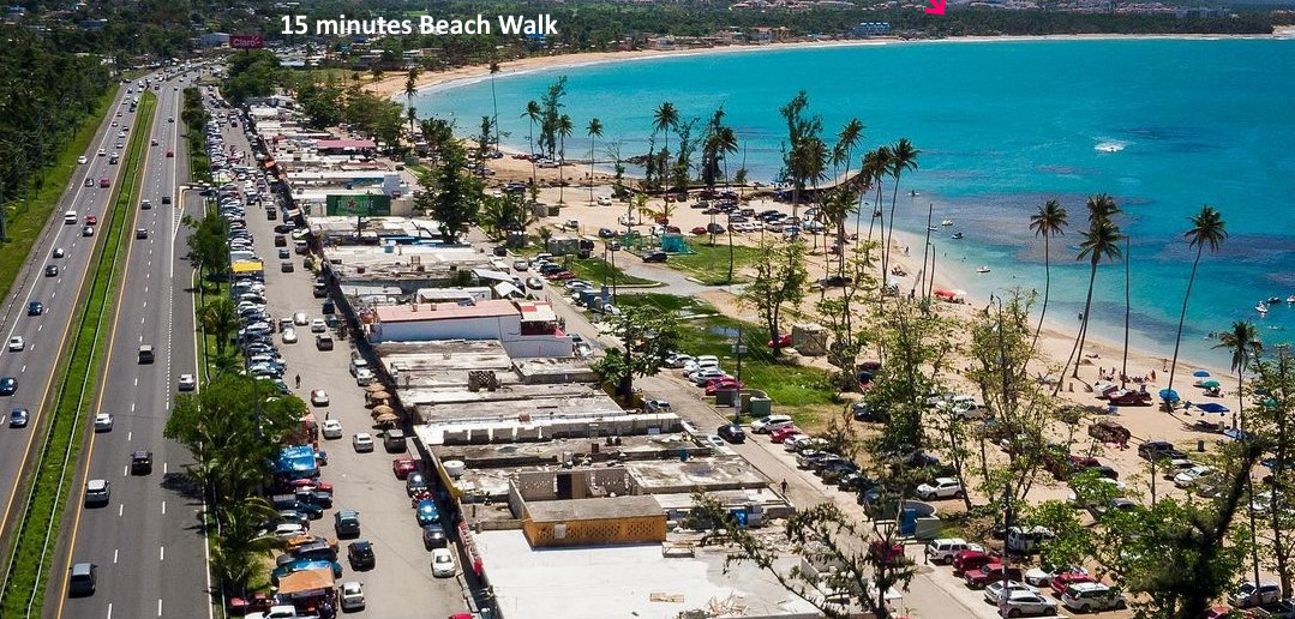 A coastal road leading to a beach area with parked cars and a view of the beach.