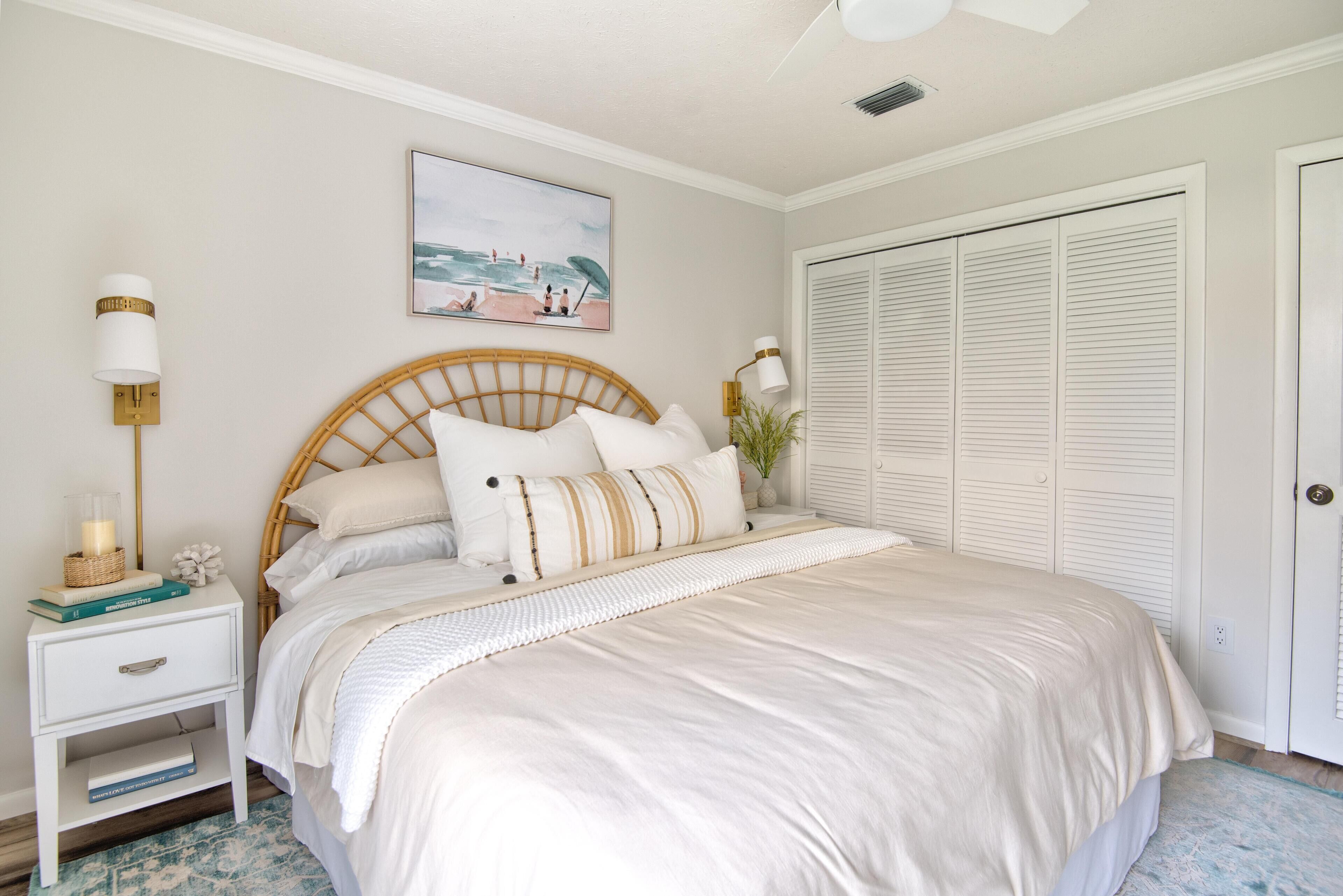 Une chambre bien rangée, avec un lit, des tables de chevet, une commode, une lampe fixée au mur, un tableau encadré et un placard.