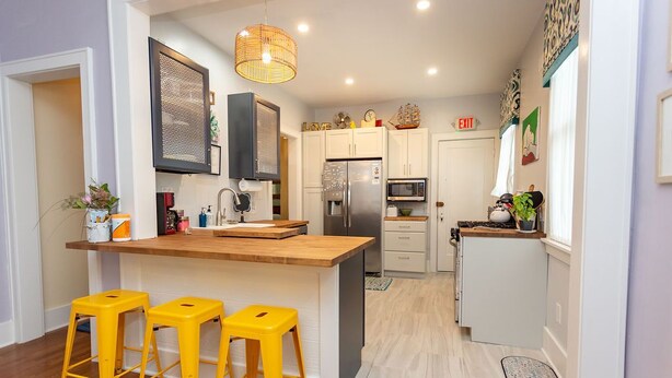 Een moderne keuken met witte kasten, een houten keukeneiland met gele krukken, een roestvrijstalen koelkast en een magnetron.