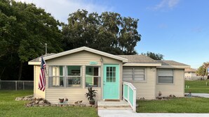 Een klein, gelijkvloers huis met een turquoise voordeur, een welkomstbord en een Amerikaanse vlag.