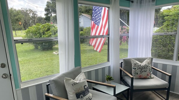 Een oranjerie met twee fauteuils, een bijzettafeltje en uitzicht op een tuin met een Amerikaanse vlag.