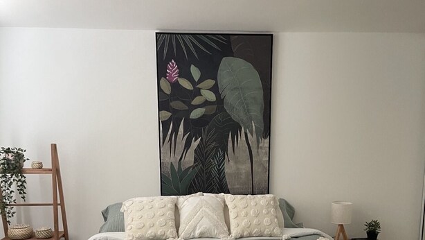 A bedroom with a bed, pillows, a blanket, a wall art piece, a bedside table, a lamp, and a small plant. - Cozy Apartment in the Heart of Rincon (Rincon)