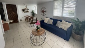 A living room with a blue sofa, a round coffee table, and a dining area with a table and chairs. - Cozy Apartment in the Heart of Rincon (Rincon)