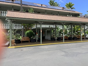 A covered outdoor area with a bench, potted plants, and a building with solar panels.