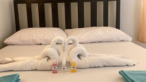 Una cama con cabecera de madera, almohadas blancas y toallas dispuestas en forma de cisnes. Hay tres botellas de champú y una toalla azul sobre la cama.