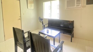 Una sala de estar con un sofá, dos sillones, una mesita y una ventana con persianas.
