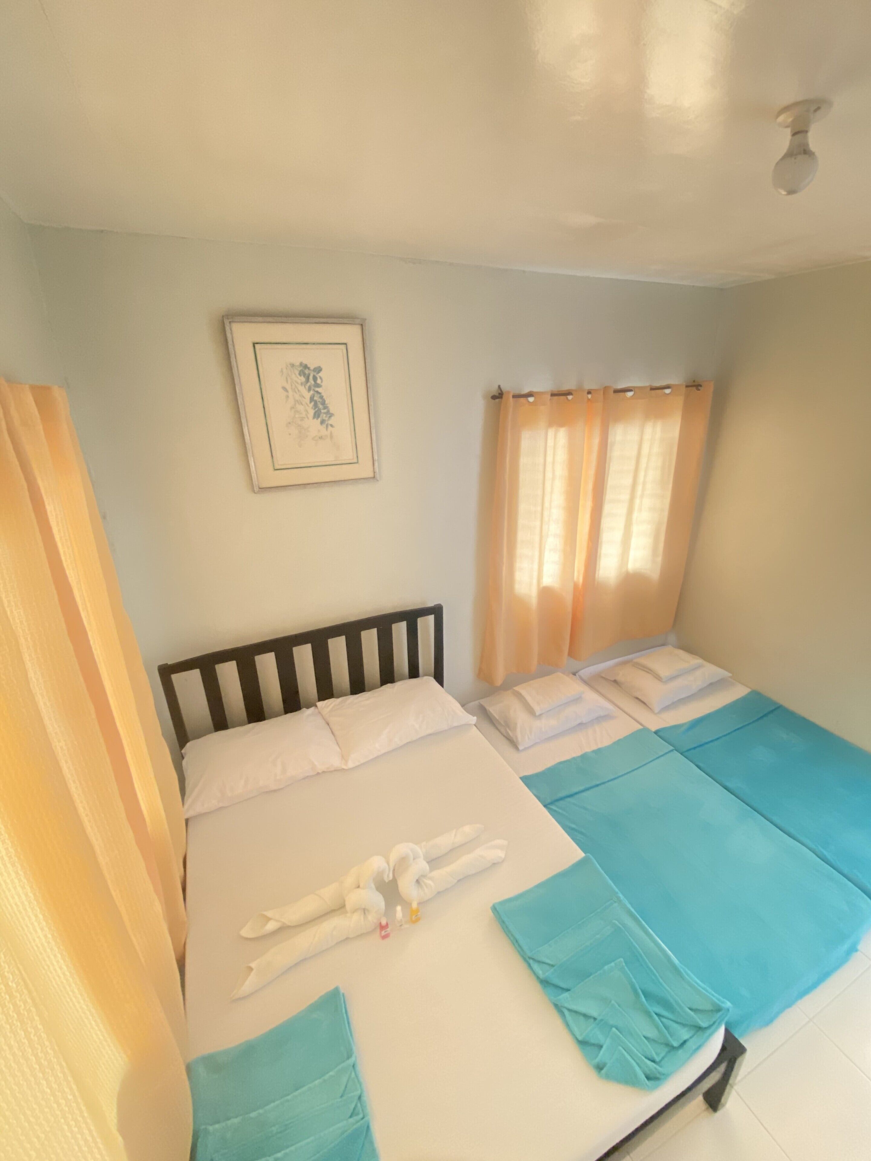 A single bed with a wooden headboard, a framed picture on the wall, and a window with curtains.