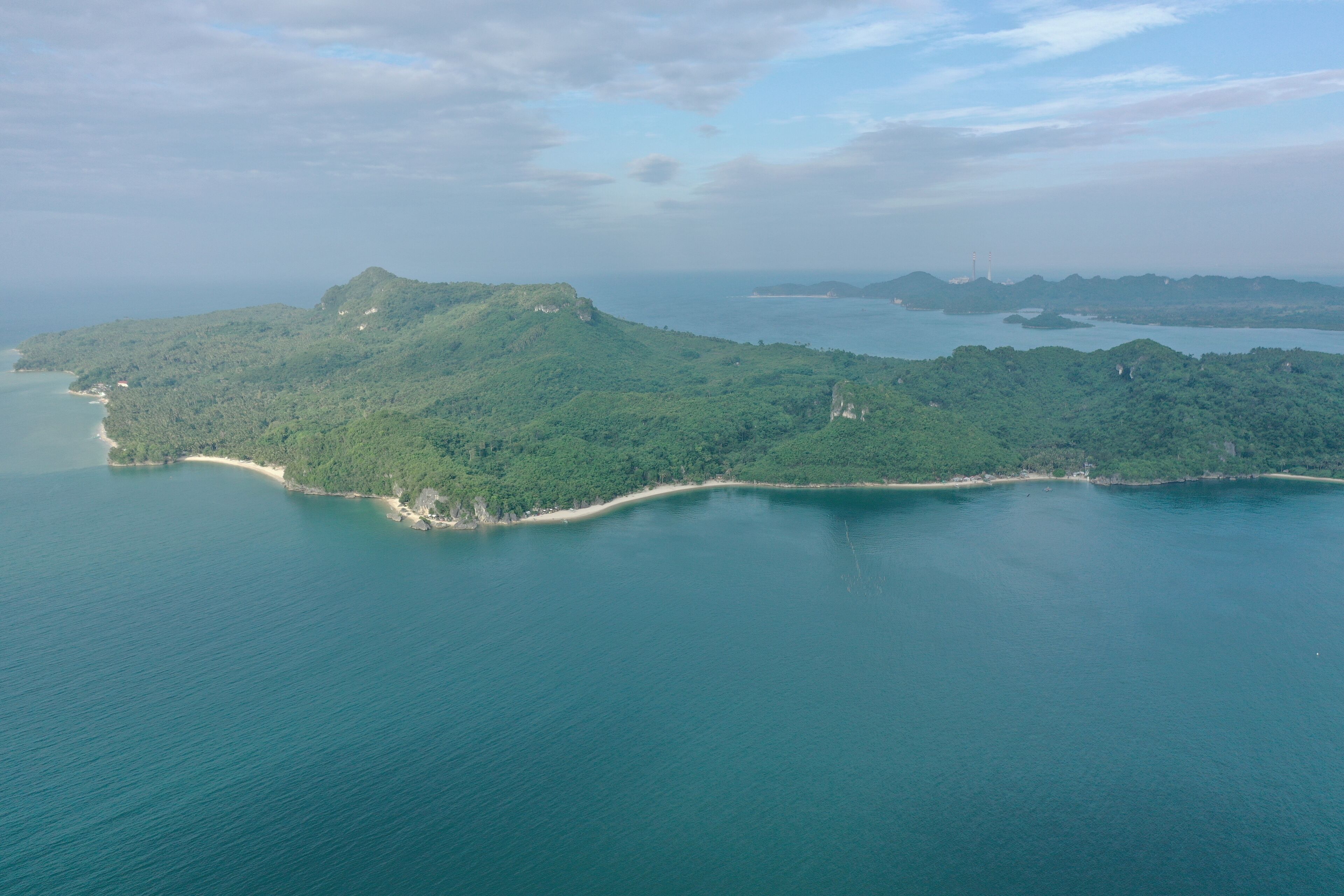 Vista aérea de una isla costera con vegetación densa, una playa de arena y un mar tranquilo.