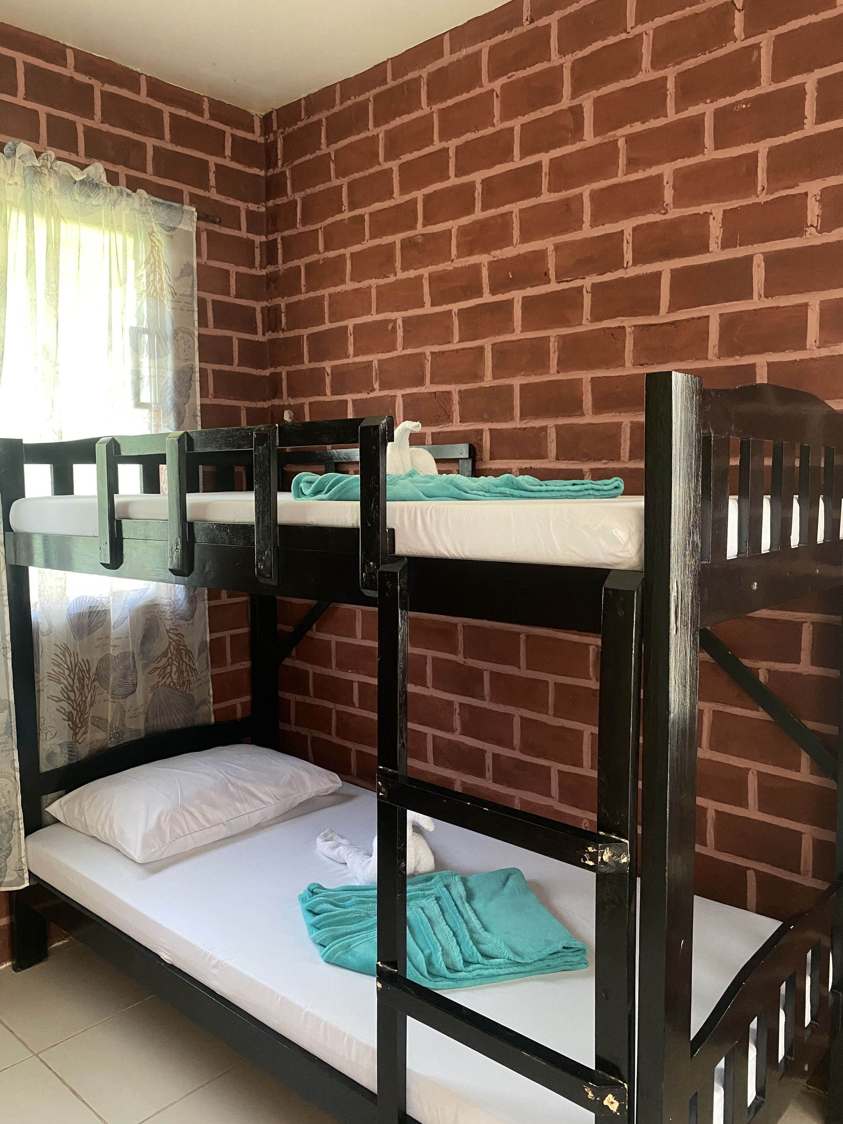 A bunk bed room with a brick wall background, a window with a curtain, and a tiled floor.