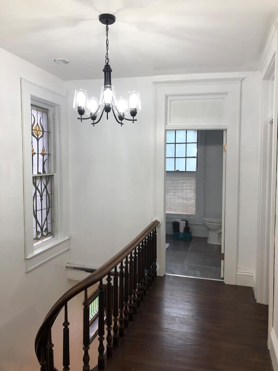 Un corridoio con una scala in legno, un lampadario e vista su un bagno.