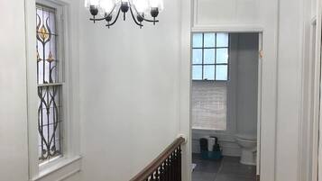 Un corridoio con una scala in legno, un lampadario e vista su un bagno.