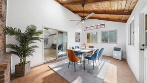 A dining area with a wooden ceiling, a ceiling fan, a large potted plant, and a dining table with chairs.