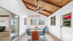 A dining area with a wooden ceiling, a table with chairs, and a view of the outdoors through windows.