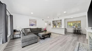 A modern living room with a grey sectional sofa, a coffee table, and a dining area with a table and chairs.