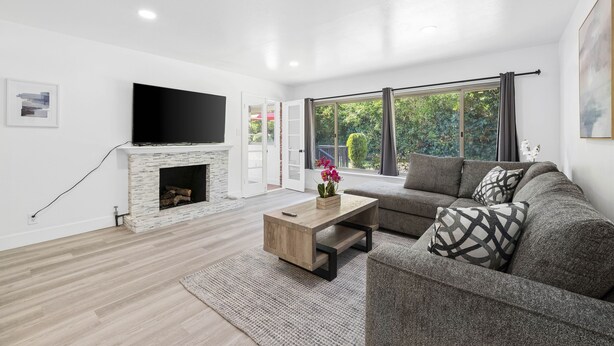 A modern living room with a fireplace, a flat-screen TV mounted above it, a sofa, and a coffee table with a vase of flowers.