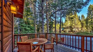 A wooden deck with a table and chairs, surrounded by a railing, overlooking a forested area. - Fully updated Truckee cabin with plenty of beds (Truckee)