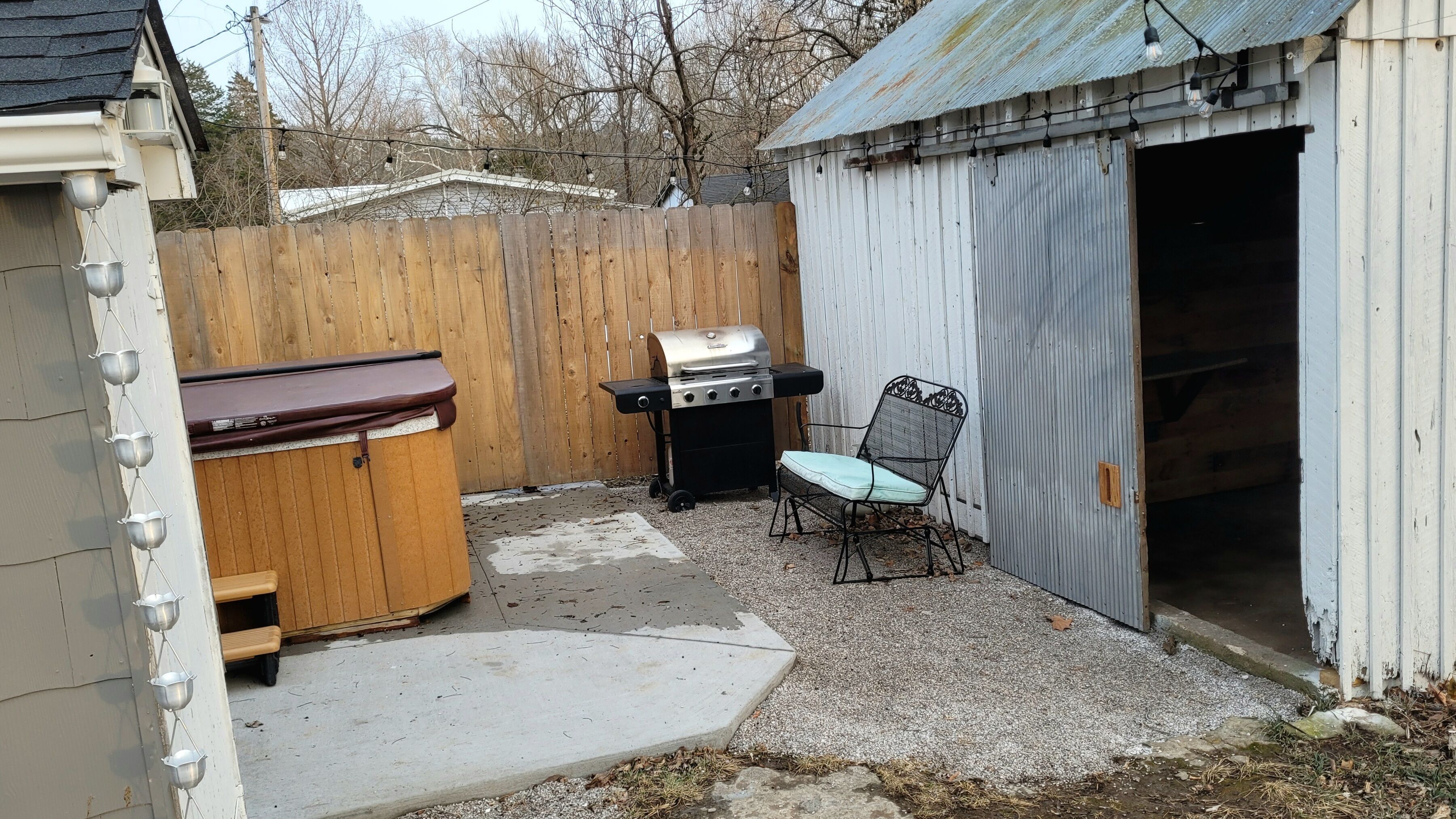 Un patio trasero con una parrilla, un banco de madera y un cobertizo.