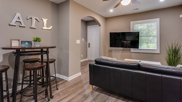 Un salon moderne avec un canapé en cuir noir, une table basse en bois et un téléviseur fixé au mur.