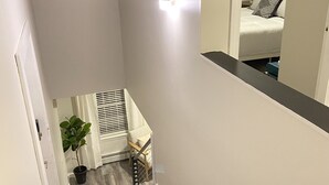Una escalera estrecha con suelo de madera, una planta en maceta y una lámpara en la pared.