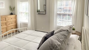 Un dormitorio con cama, cómoda, espejo y ventanas con cortinas.
