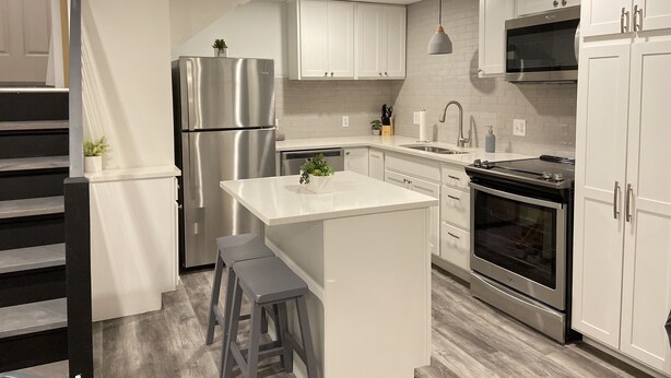 Una cocina moderna con armarios blancos, electrodomésticos de acero inoxidable y una isla central con taburetes.
