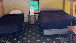 A cozy attic bedroom with two beds, a small wooden table, and a wall-mounted TV. - Base Camp Glamping @ Hidden Ridge (Saint Johnsbury)
