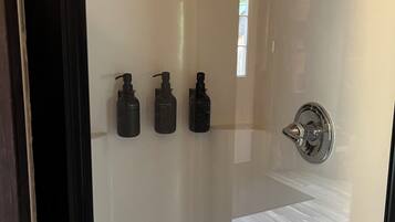 A modern bathroom with a glass shower enclosure, a toilet, and three bottles of toiletries on the wall.