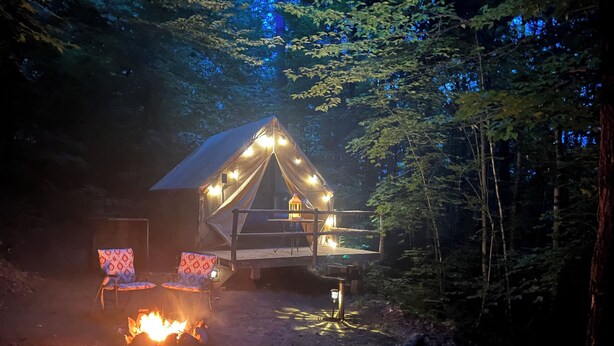 A tent with a fire in front, surrounded by trees. - Base Camp Glamping @ Hidden Ridge (Saint Johnsbury)