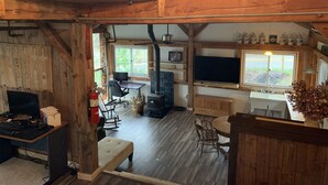 A rustic cabin interior with a wooden dining table, a sofa, a fireplace, and a television. - Base Camp Glamping @ Hidden Ridge (Saint Johnsbury)