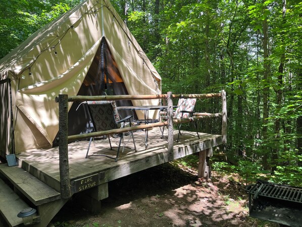 A tent with a fire safety sign, a wooden deck, and two chairs.