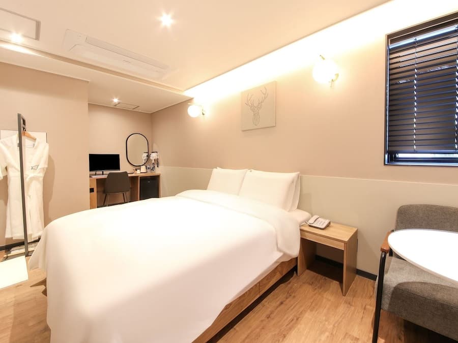 Una habitación de hotel con cama, mesita de noche, silla, escritorio y bata colgada en un perchero.