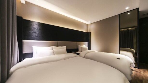 Ein modernes Hotelzimmer mit einem großen Bett, einem dunklen Kopfteil und einem Spiegel an der Wand.