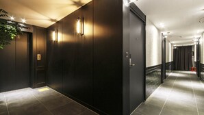 Ein moderner Hotelkorridor mit dunklen Wänden, eingelassener Beleuchtung und einem gefliesten Boden.