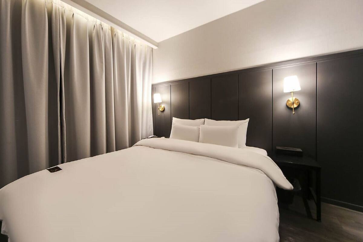Ein modernes Hotelzimmer mit einem großen Bett, einem dunklen Holz-Kopfteil und zwei Wandleuchten.