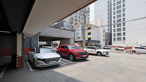 En parkeringsplats med flera bilar, bland annat en röd SUV och en vit sedan, parkerade under en överbyggnad.