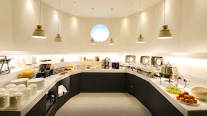 A modern breakfast bar with a curved design, equipped with various food and beverage stations, including a coffee maker, toaster, and fruit display. - Ocean the point Hotel (Busan)