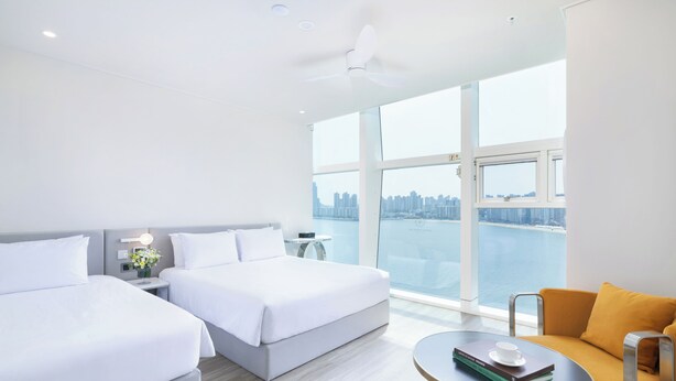 Une chambre d’hôtel avec deux lits, un coin salon avec une table et une vue sur le paysage urbain et l’eau.