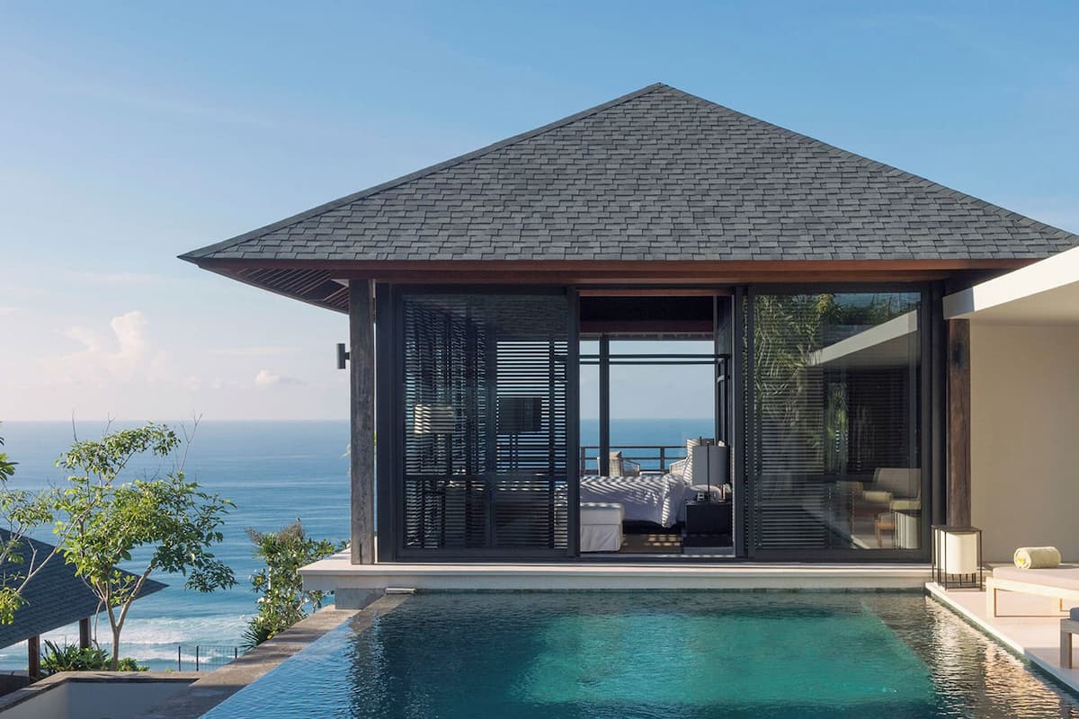 A modern villa with a private pool, large windows, and a view of the ocean.