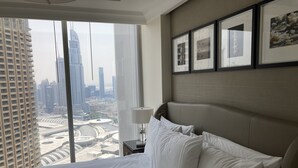 A hotel room with a large bed, a nightstand, a lamp, and a view of a cityscape through floor-to-ceiling windows. - Ultimate Luxury Address Boulevard Dubai - 3 Bedrooms (Dubai)