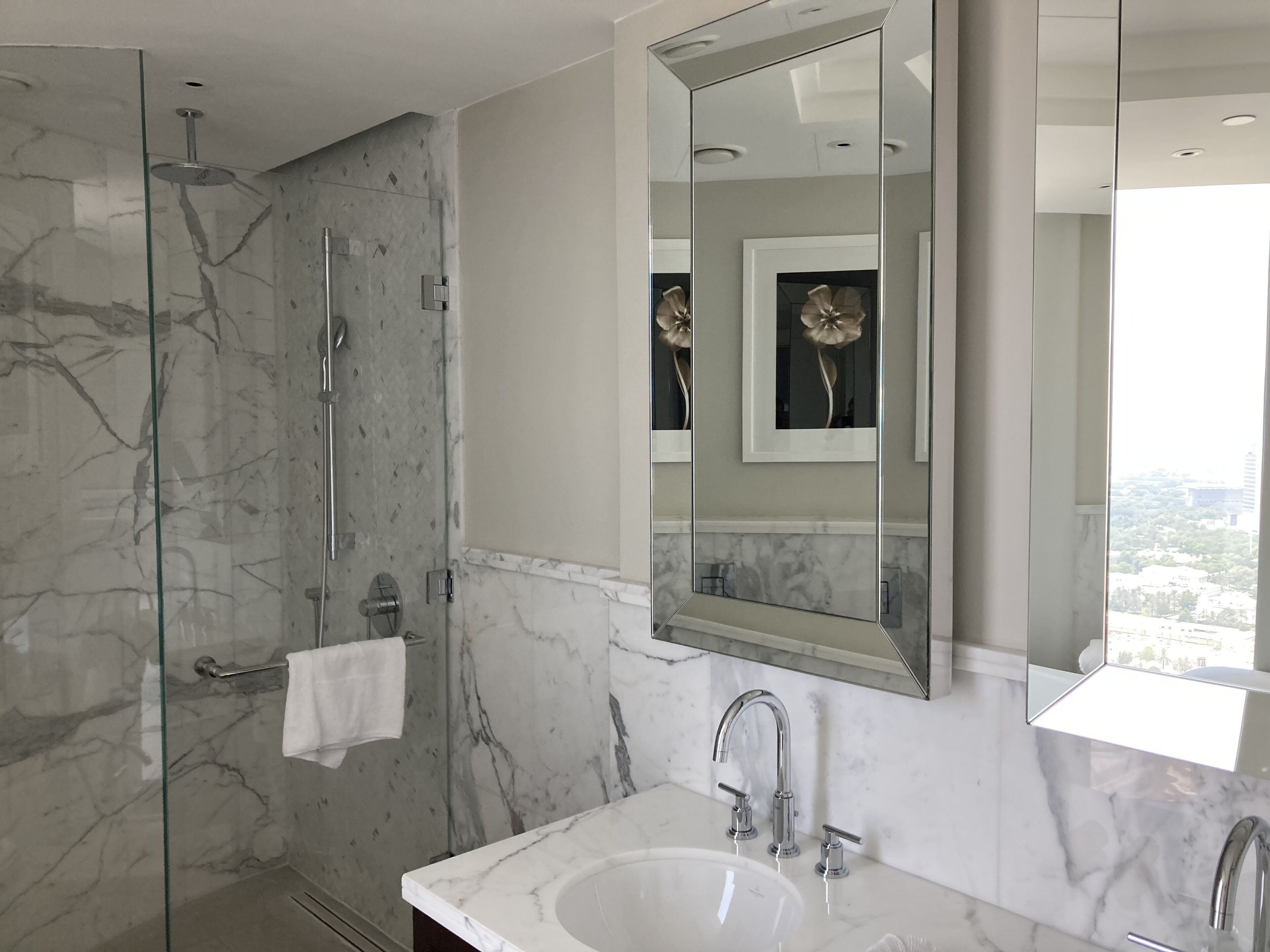 A modern bathroom with a glass-enclosed shower, a large mirror, and a marble sink.