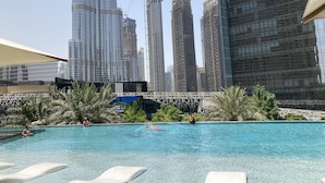 A swimming pool with clear blue water, surrounded by palm trees and modern buildings in the background. - Ultimate Luxury Address Boulevard Dubai - 3 Bedrooms (Dubai)