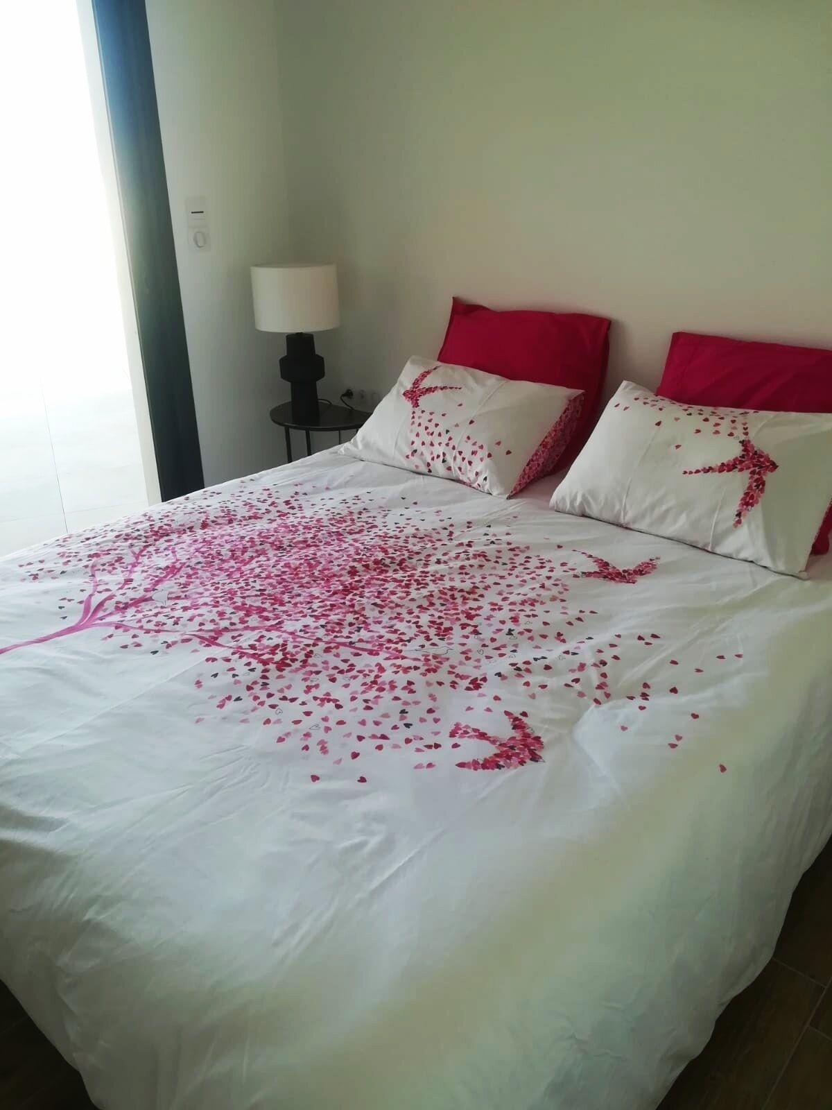 A bed with a white bedspread and pink heart-shaped decorations.