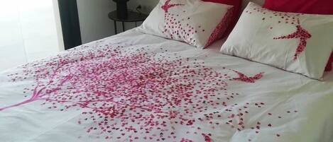 A bed with a white bedspread and pink heart-shaped decorations.
