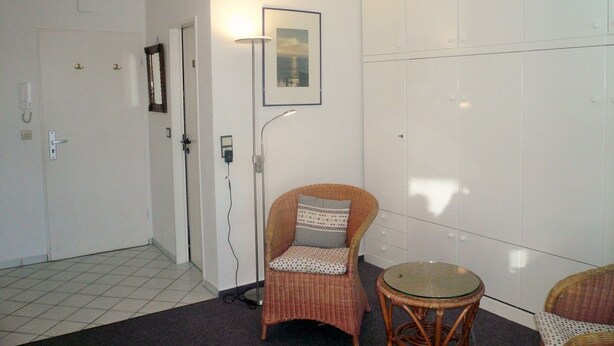 A room with a wicker chair, a small round table, a floor lamp, and a wardrobe. - Sievers 37, Deutschland (Sylt)