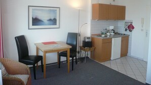 A compact kitchen with wooden cabinets, a small dining table with chairs, and a single artwork on the wall. - Sievers 37, Deutschland (Sylt)
