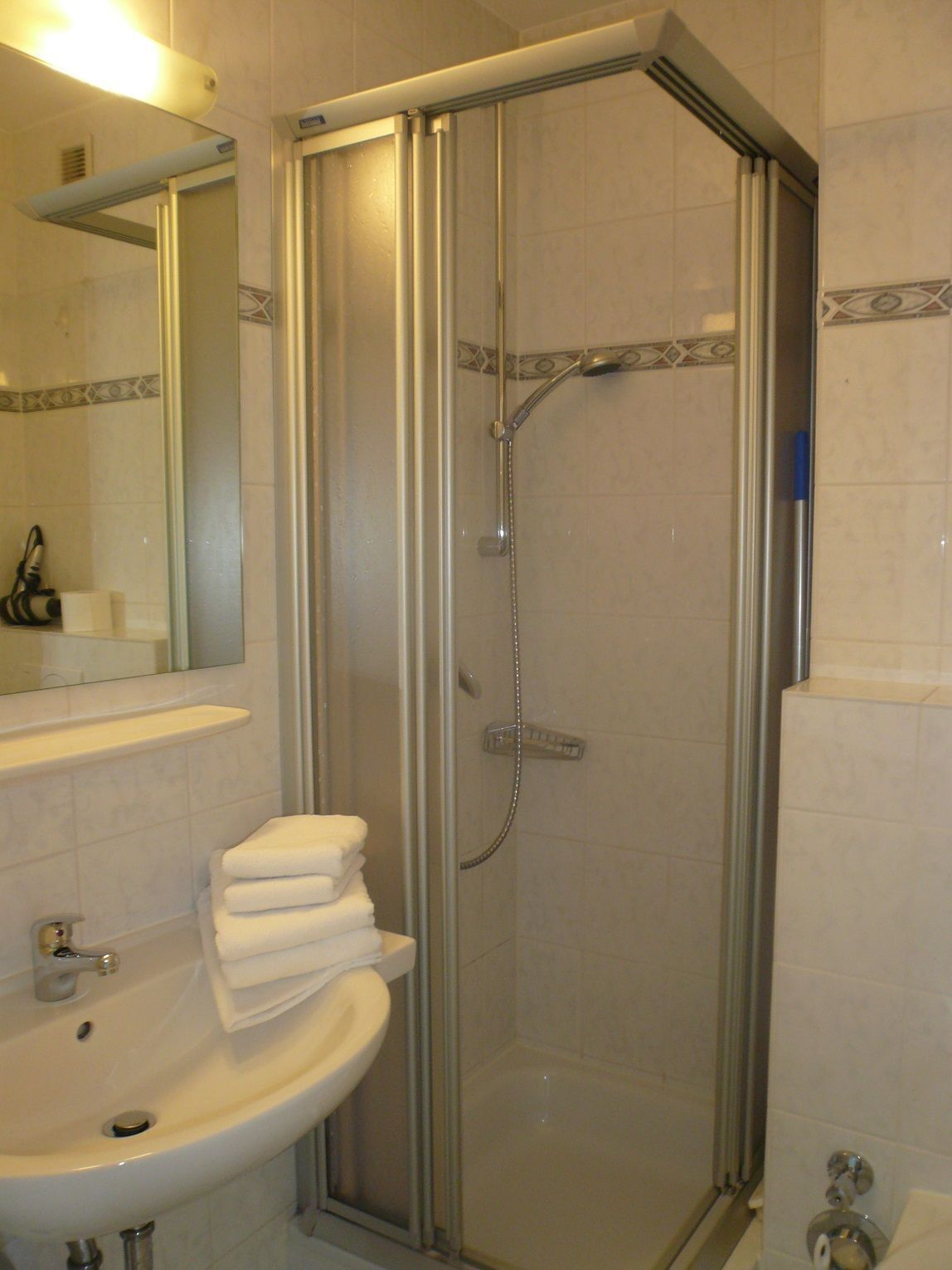 A bathroom with a glass-enclosed shower, a sink with a mirror, and a stack of white towels.
