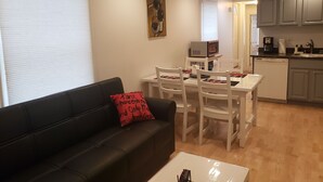 A living room with a black sofa, a white coffee table, and a dining area with white chairs and a small table.