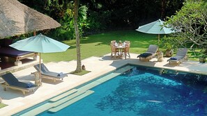 A pool area with lounge chairs, umbrellas, and a dining table.